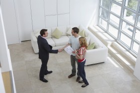 A man in a suit shakes hands with a couple in a white room